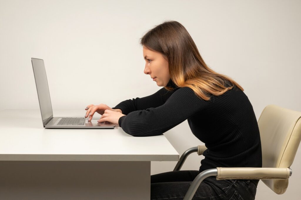 Young woman in slouching position sitting in office room, working with laptop