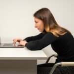 Young woman in slouching position sitting in office room, working with laptop